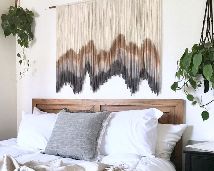Un tapiz de macramé decorando la pared de encima de la cama.