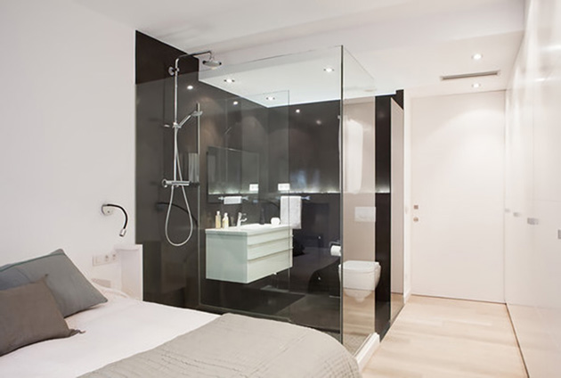 Un baño abierto al dormitorio separado por tabiques de cristal