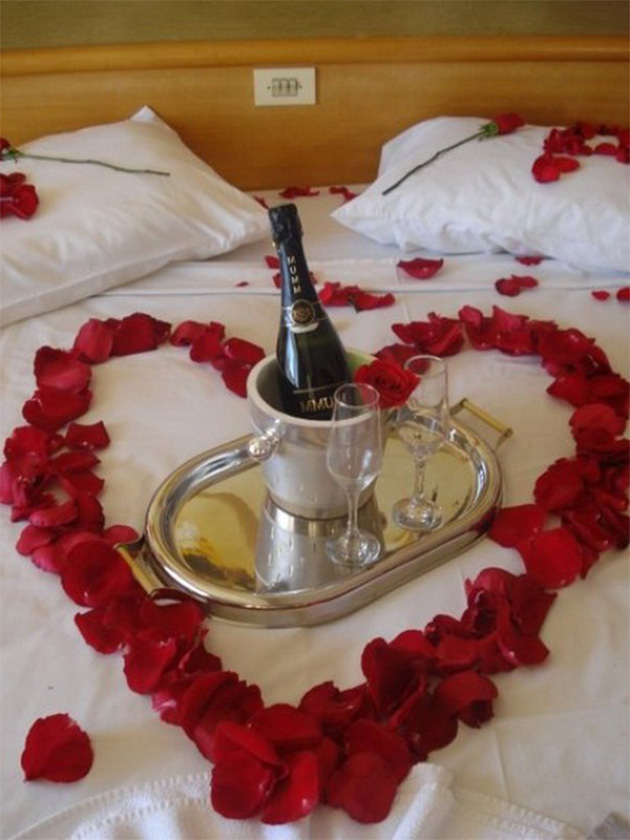 Una cama decorada con pétalos de rosas y champan