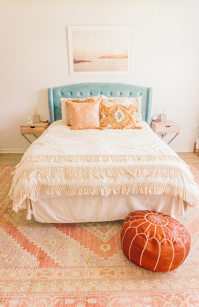 Pie de cama decorado con una alfombra y un puf